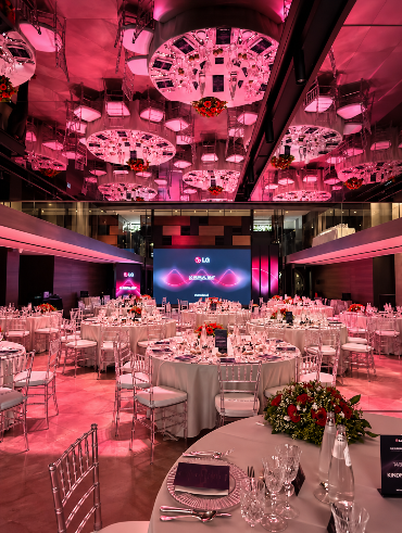 Sala allestita per l'evento LG Human Beat presso Spazio Gessi, con tavoli apparecchiati, illuminazione scenografica rosa e ledwall LG.